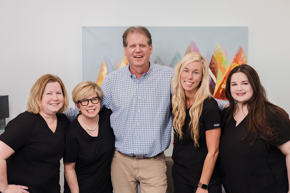 A group of five people wearing purple scrubs posing with an older man who is sitting on a bench behind them.